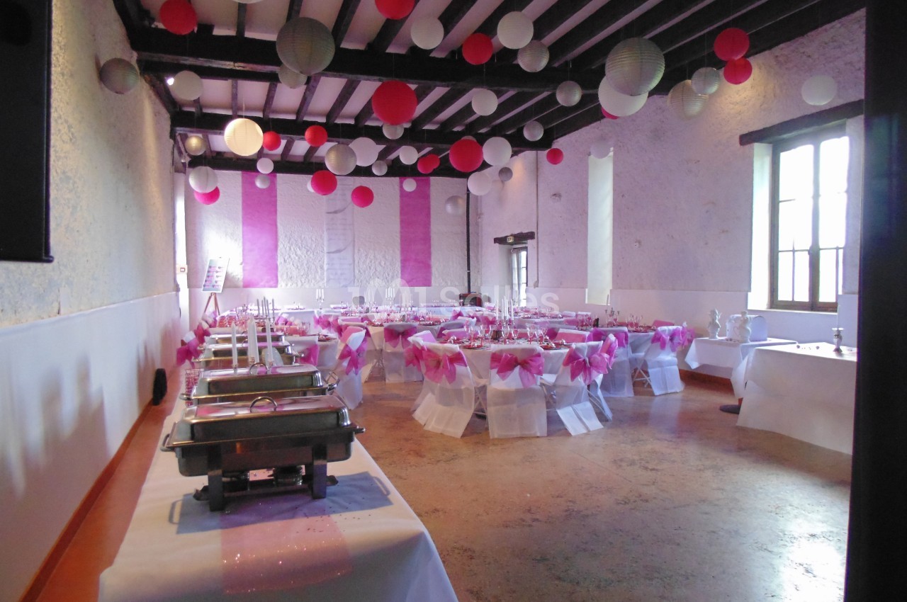 Salle de réception décorée avec des nappes blanches, des rubans roses et des lanternes suspendues au plafond.