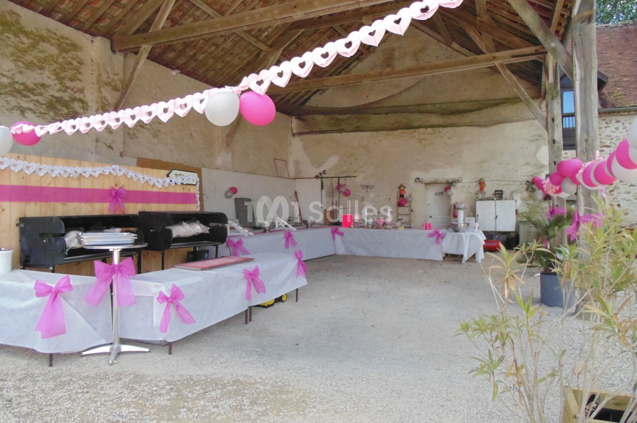 Salle décorée avec des guirlandes roses et blanches, tables dressées pour un buffet sous une charpente en bois.