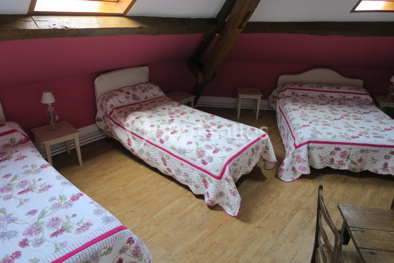 Chambre mansardée avec trois lits simples, couvre-lits fleuris, murs roses et poutres apparentes en bois.