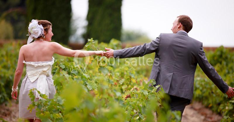 Un couple en tenue de mariage se tient la main en marchant dans un vignoble verdoyant.