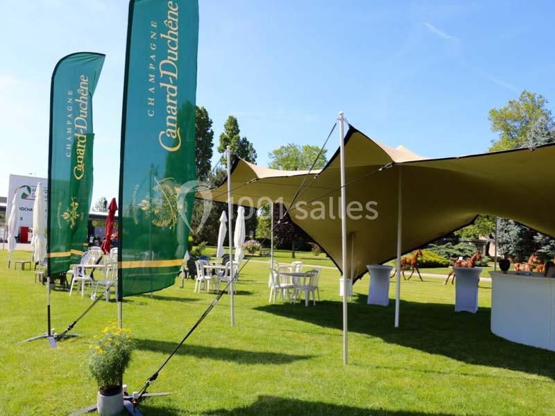Tentes et tables installées sur une pelouse avec des drapeaux ’Champagne Canard-Duchêne’ visibles en premier plan.