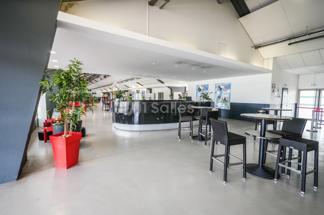 Intérieur spacieux avec comptoir noir, tables hautes, plantes en pots rouges et murs blancs décorés.