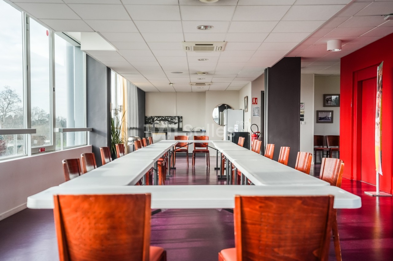 Salle de réunion lumineuse avec une grande table en U entourée de chaises en bois, sol violet et mur rouge.