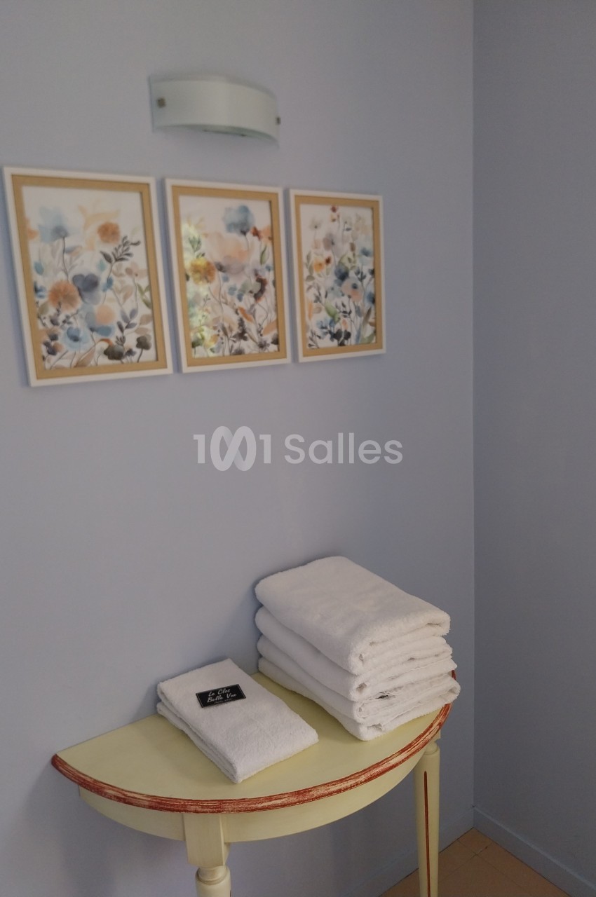 Table étroite avec des serviettes blanches pliées, une petite étiquette noire et trois cadres floraux accrochés au mur.