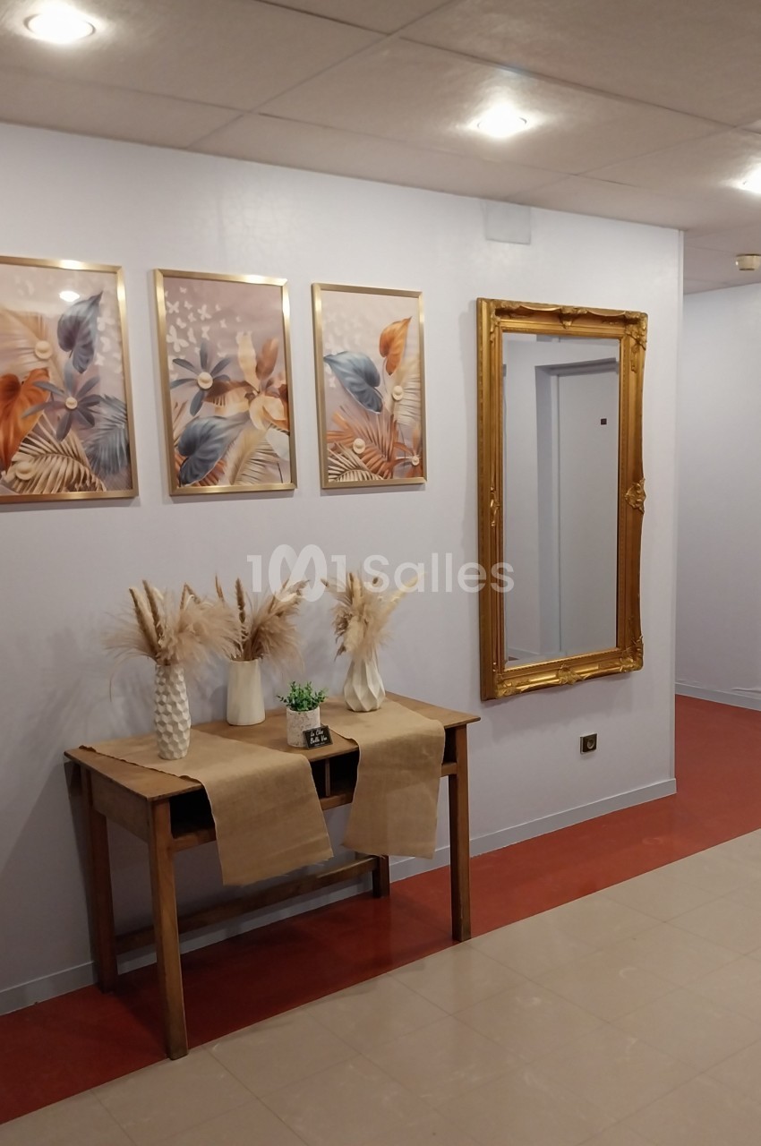 Table en bois décorée de vases avec des fleurs séchées, miroir doré et tableaux floraux accrochés au mur.