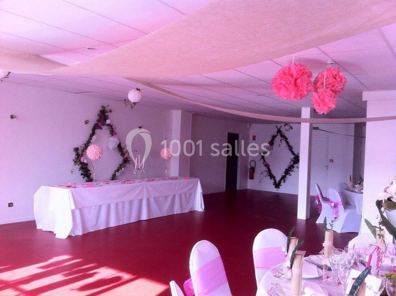 Salle de réception décorée avec des guirlandes, fleurs suspendues et une table longue ornée de nappes blanches.