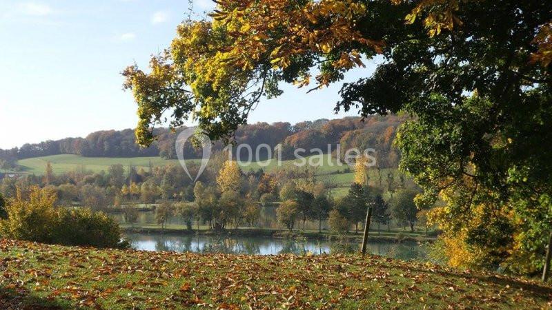 Paysage automnal avec un lac entouré de collines boisées et d'arbres aux feuilles colorées.