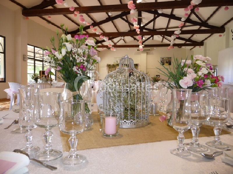 Décoration de table avec fleurs, verres, bougies et une cage métallique au centre dans une salle lumineuse.