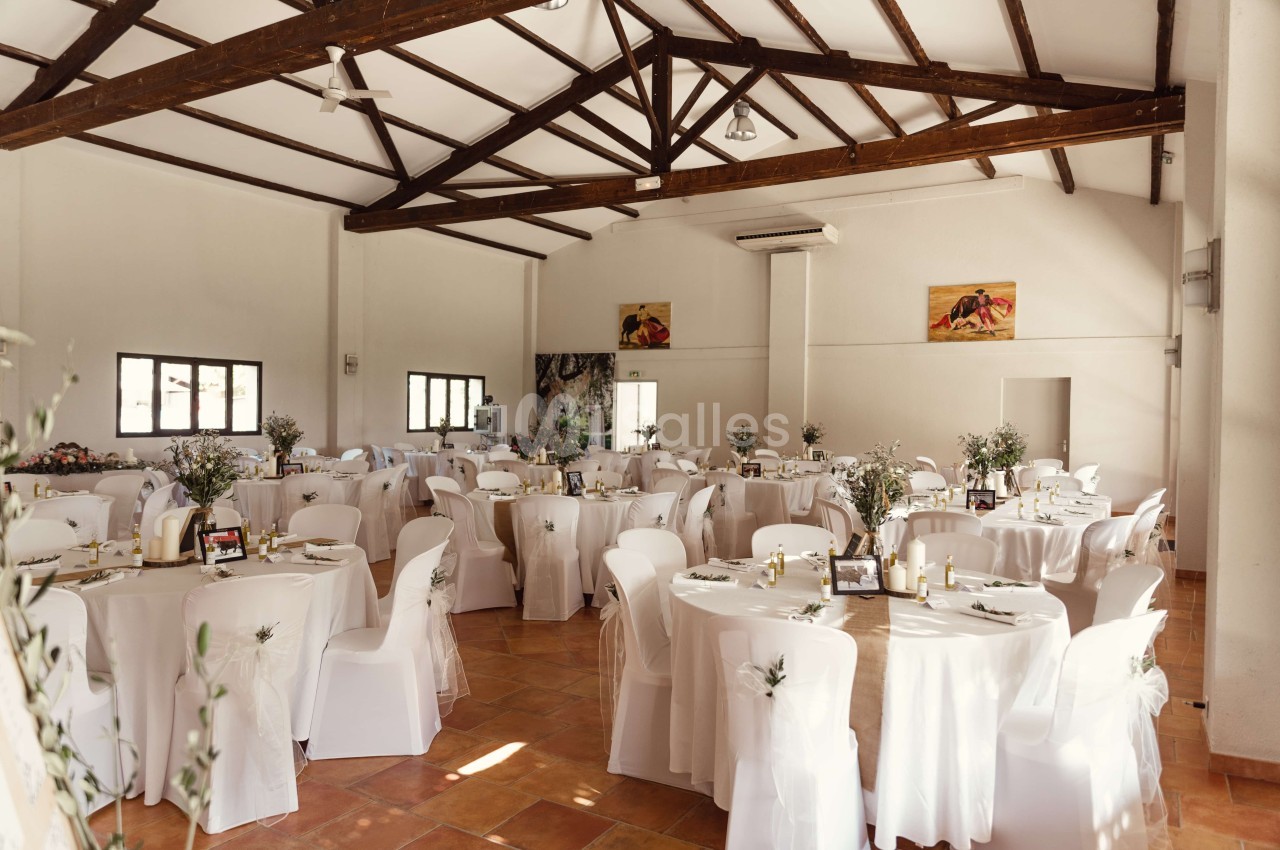 Salle de réception lumineuse avec des tables rondes décorées de nappes blanches et de centres de table floraux.