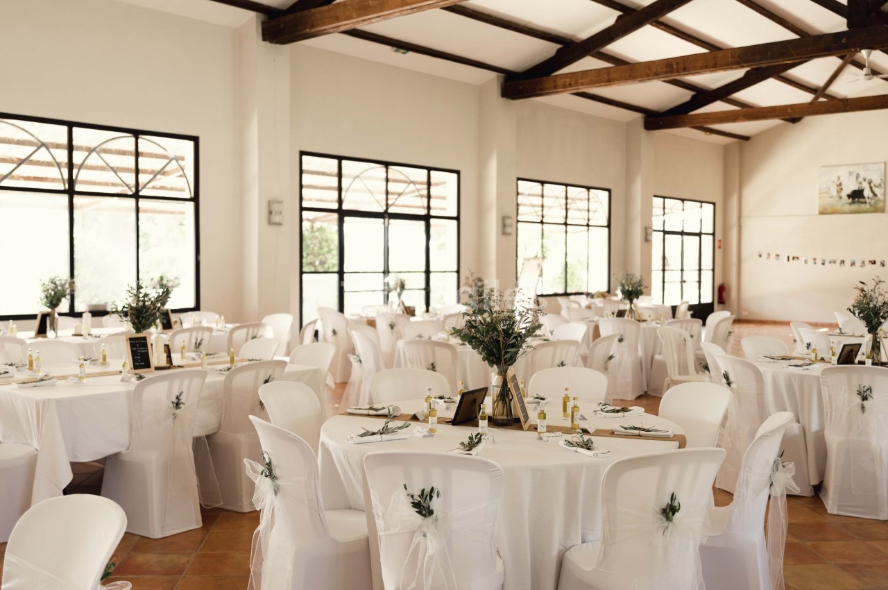 Salle de réception lumineuse avec des tables rondes décorées de nappes blanches, centres de table et chaises assorties.