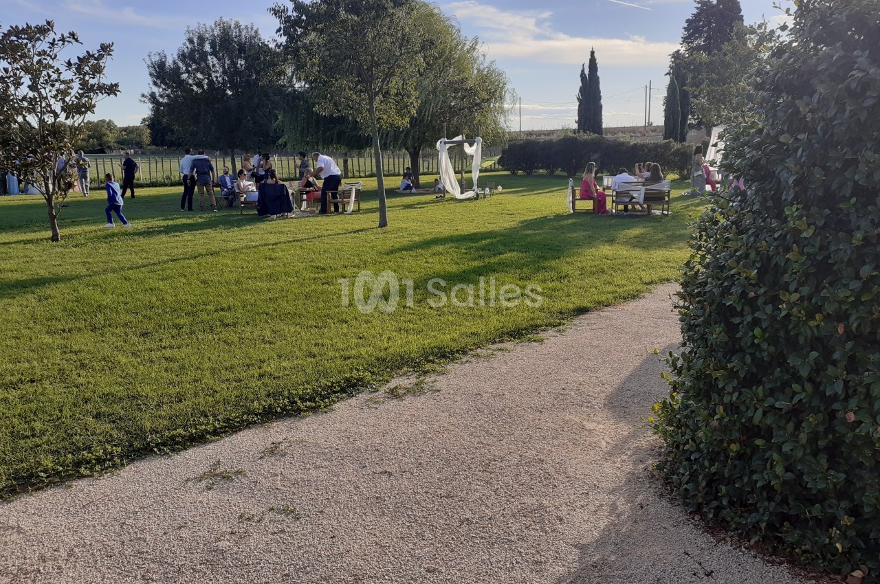 Des personnes se détendent et discutent dans un parc verdoyant avec des arbres, des tables et des structures blanches.