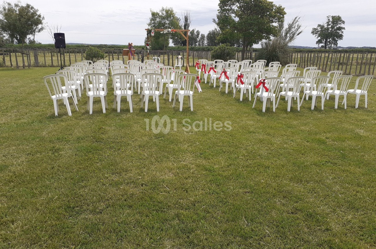 Chaises blanches disposées en rangées sur une pelouse, formant une allée centrale décorée pour une cérémonie en plein air.