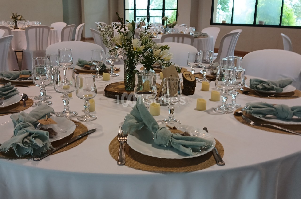 Table dressée pour un événement, avec nappes blanches, serviettes vertes, verres, couverts et centre de table floral.