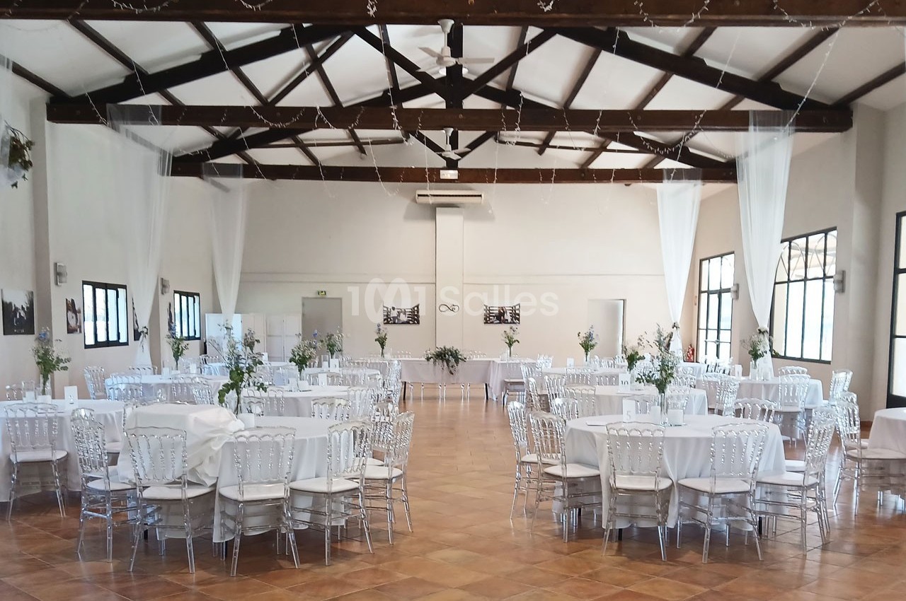 Salle de réception lumineuse avec tables rondes décorées de nappes blanches et chaises transparentes.