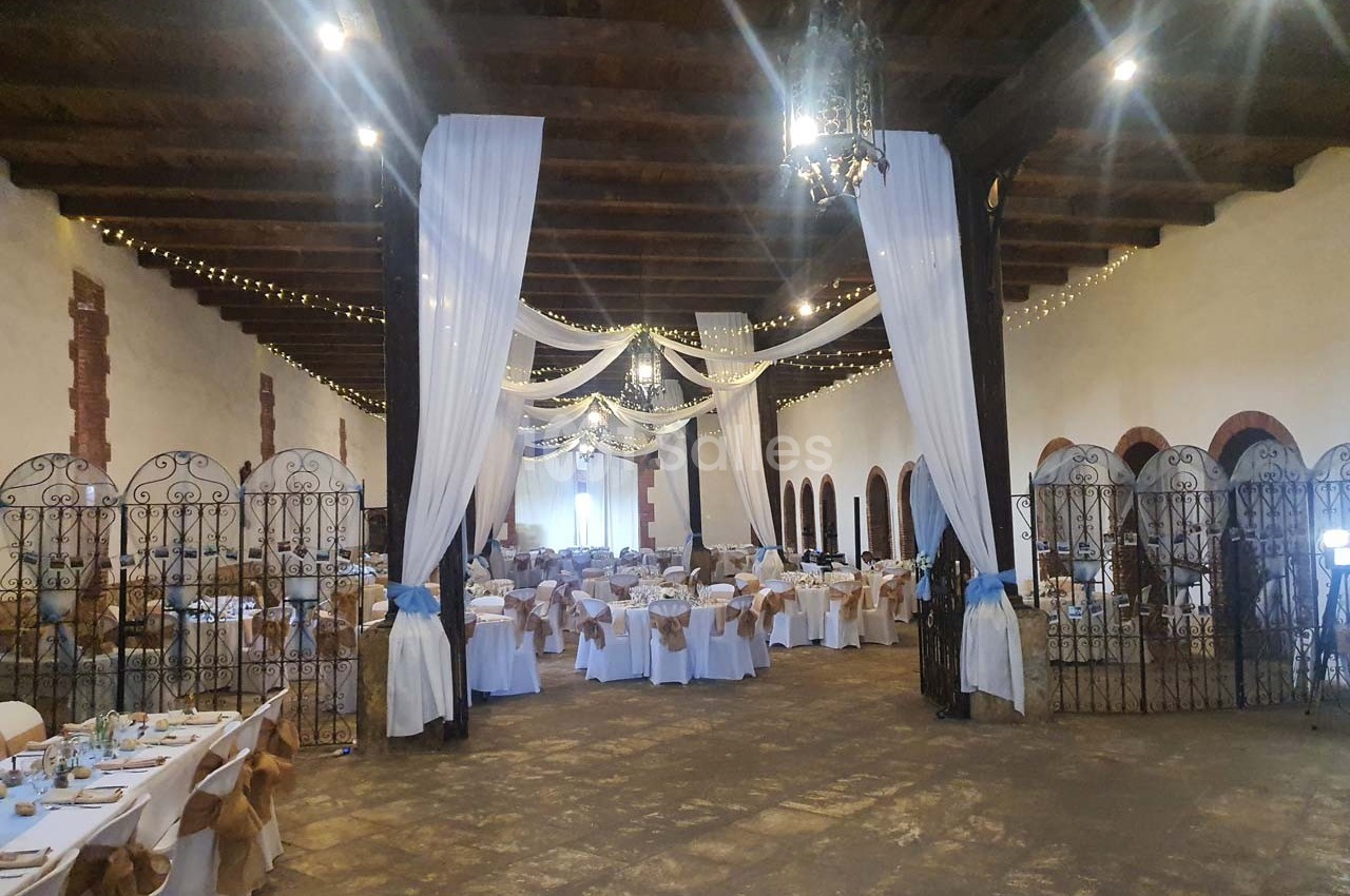 Salle de réception décorée avec des tables dressées, des chaises ornées de nœuds et des drapés suspendus au plafond.