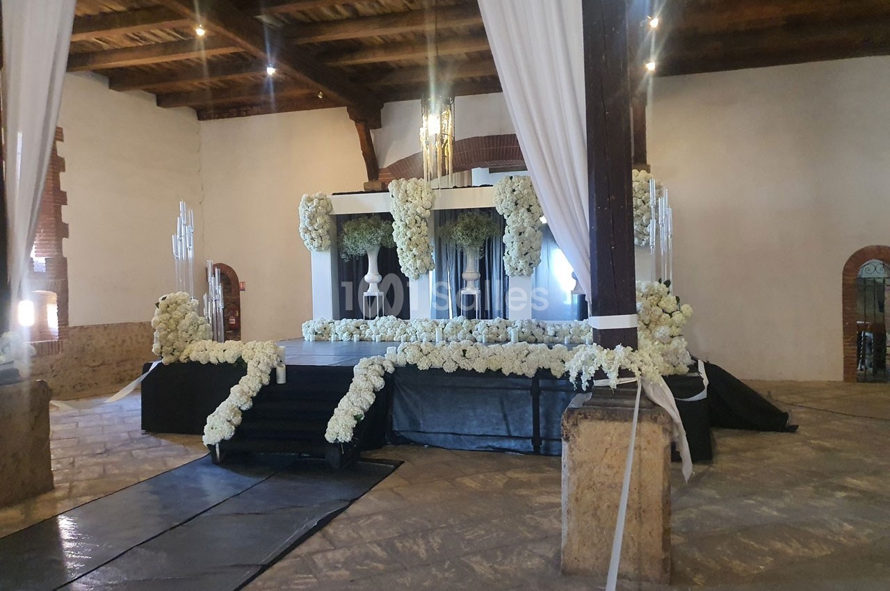 Scène décorée de fleurs blanches dans une salle avec plafond en bois et murs en pierre.