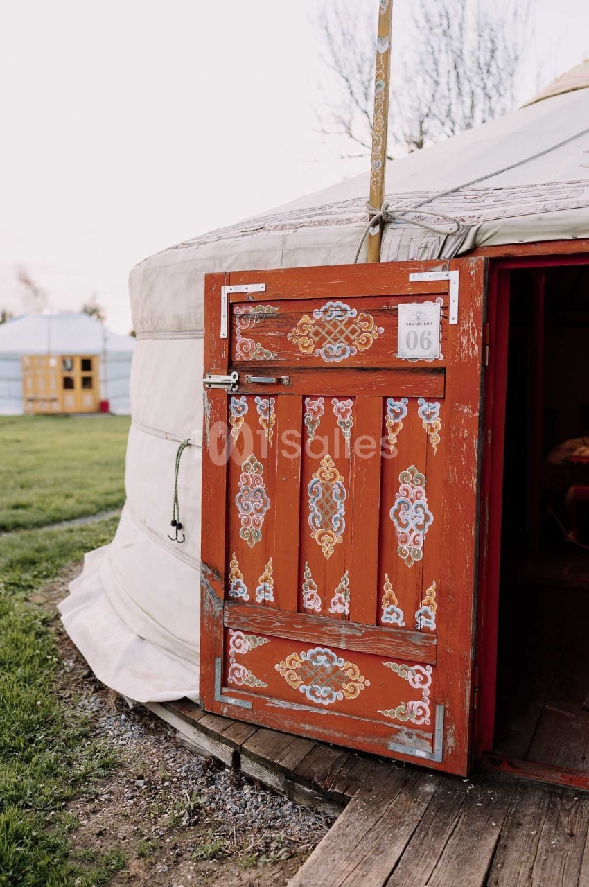 Porte en bois ornée de motifs colorés, entrouverte sur une yourte traditionnelle dans un cadre extérieur verdoyant.