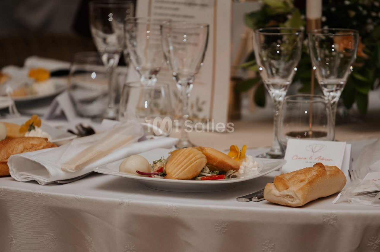 Table dressée avec assiettes garnies, verres à pied, serviettes pliées et pain, dans un cadre de réception élégante.