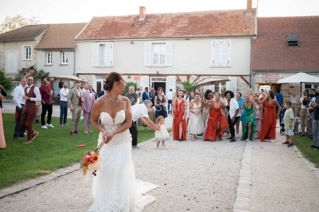 Une mariée lance son bouquet devant un groupe d'invités rassemblés dans une cour extérieure.