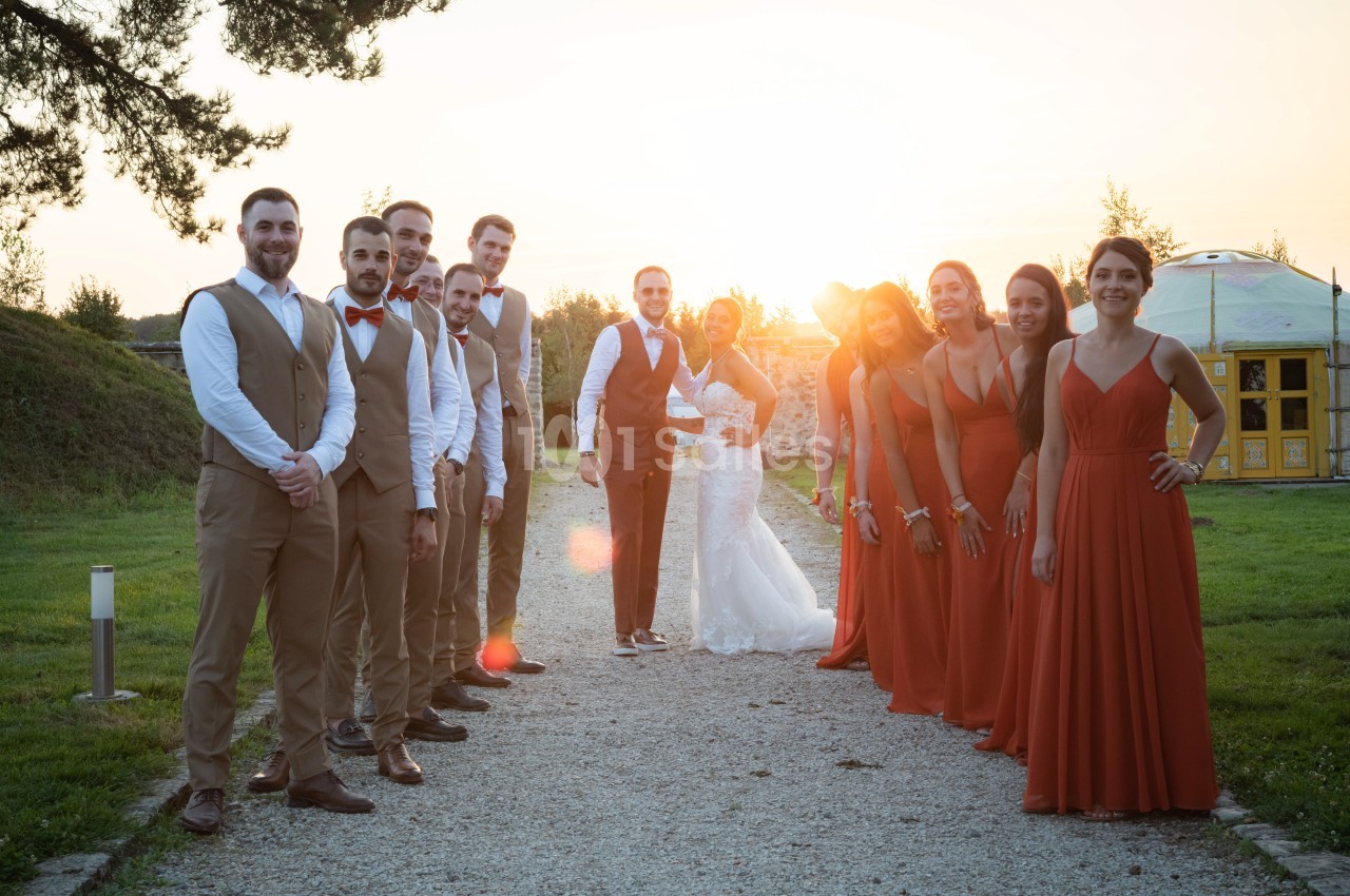 Un couple de mariés entouré de leurs témoins et demoiselles d'honneur posant en extérieur au coucher du soleil.