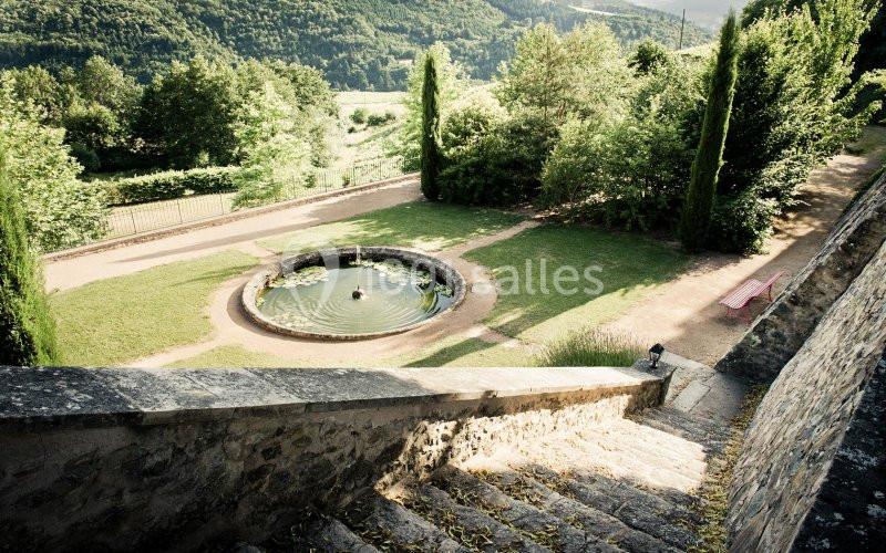 Vue depuis des escaliers en pierre sur un jardin avec une fontaine circulaire entourée de pelouse et d'arbres.