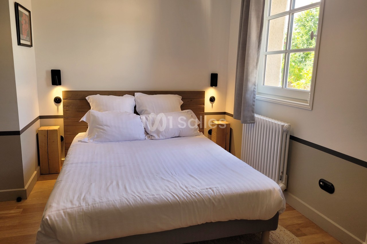 Chambre lumineuse avec un lit double, deux tables de chevet en bois, et une fenêtre donnant sur un jardin.
