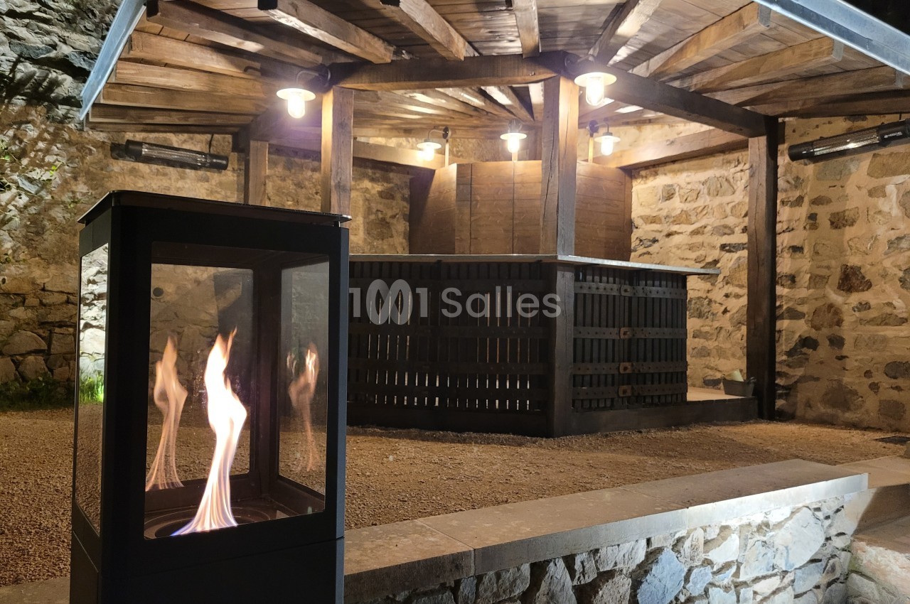 Abri en pierre et bois éclairé, avec un poêle à gaz moderne en premier plan et des flammes visibles.