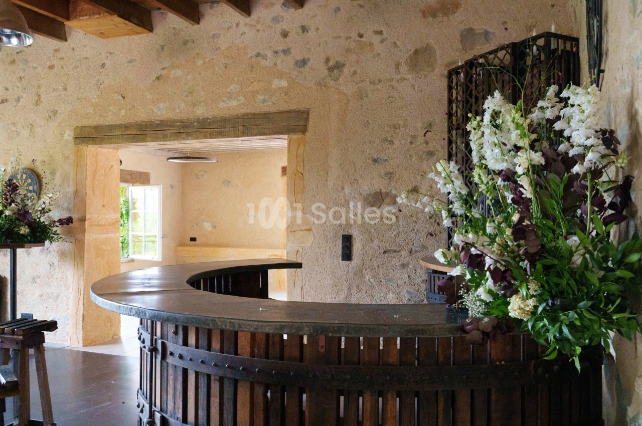 Comptoir en bois courbé dans une pièce en pierre avec des fleurs blanches et violettes en décoration.