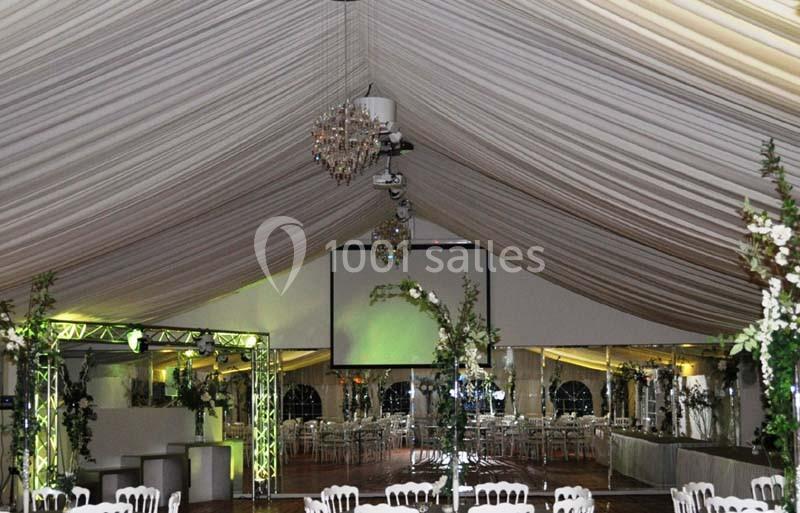 Intérieur d'une tente de réception décorée avec des lustres, des drapés au plafond et des tables dressées en arrière-plan.