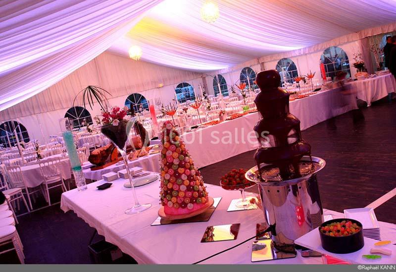 Buffet de desserts dans une tente éclairée, avec fontaine de chocolat et pièce montée de macarons.