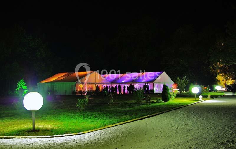 Tente éclairée aux couleurs vives dans un jardin la nuit, entourée de lampes sphériques et d'allées.