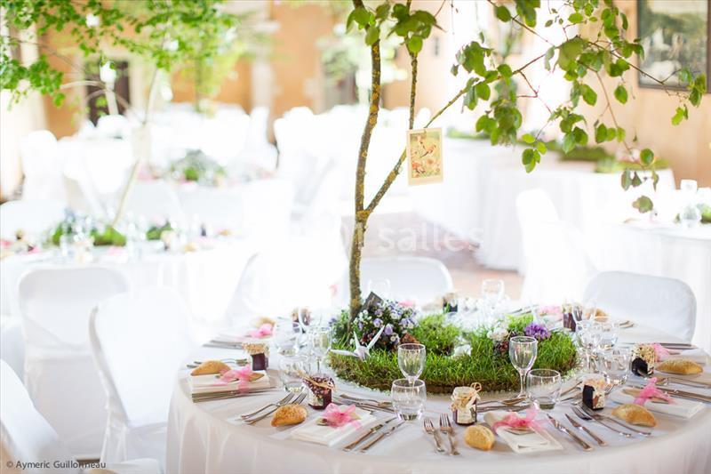 Table décorée pour un événement, ornée de verdure, couverts disposés autour et ambiance lumineuse en extérieur.