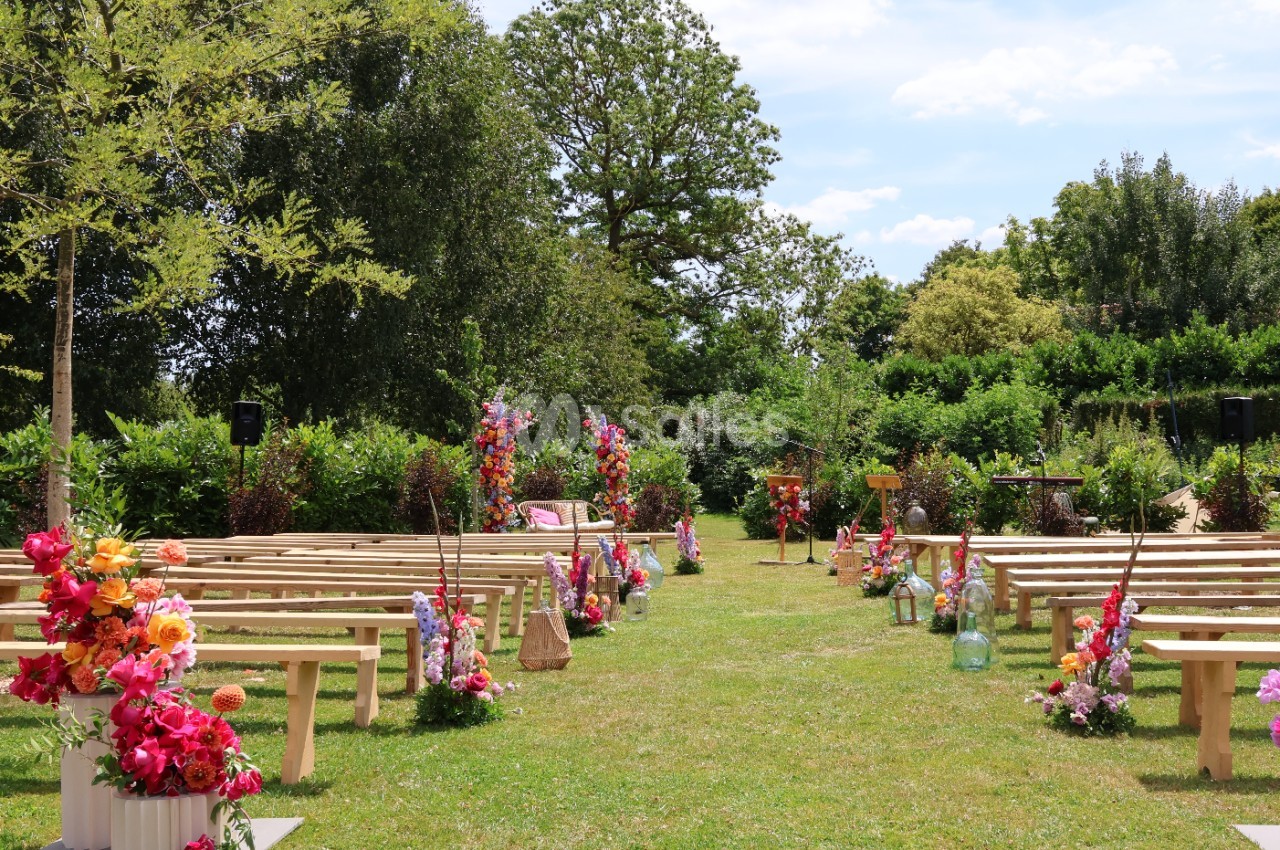 Allée centrale bordée de bancs en bois et de compositions florales colorées, dans un jardin verdoyant.