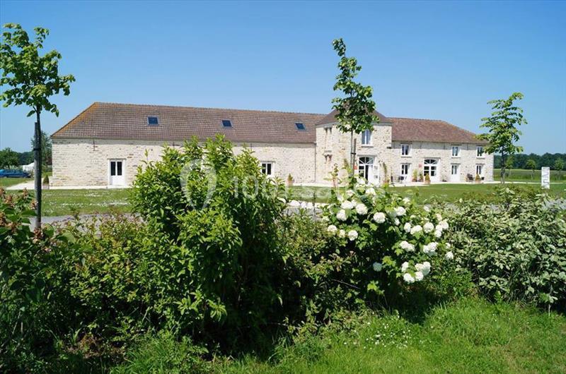 Bâtiment en pierre clair entouré de verdure, avec des arbustes et des fleurs blanches au premier plan.