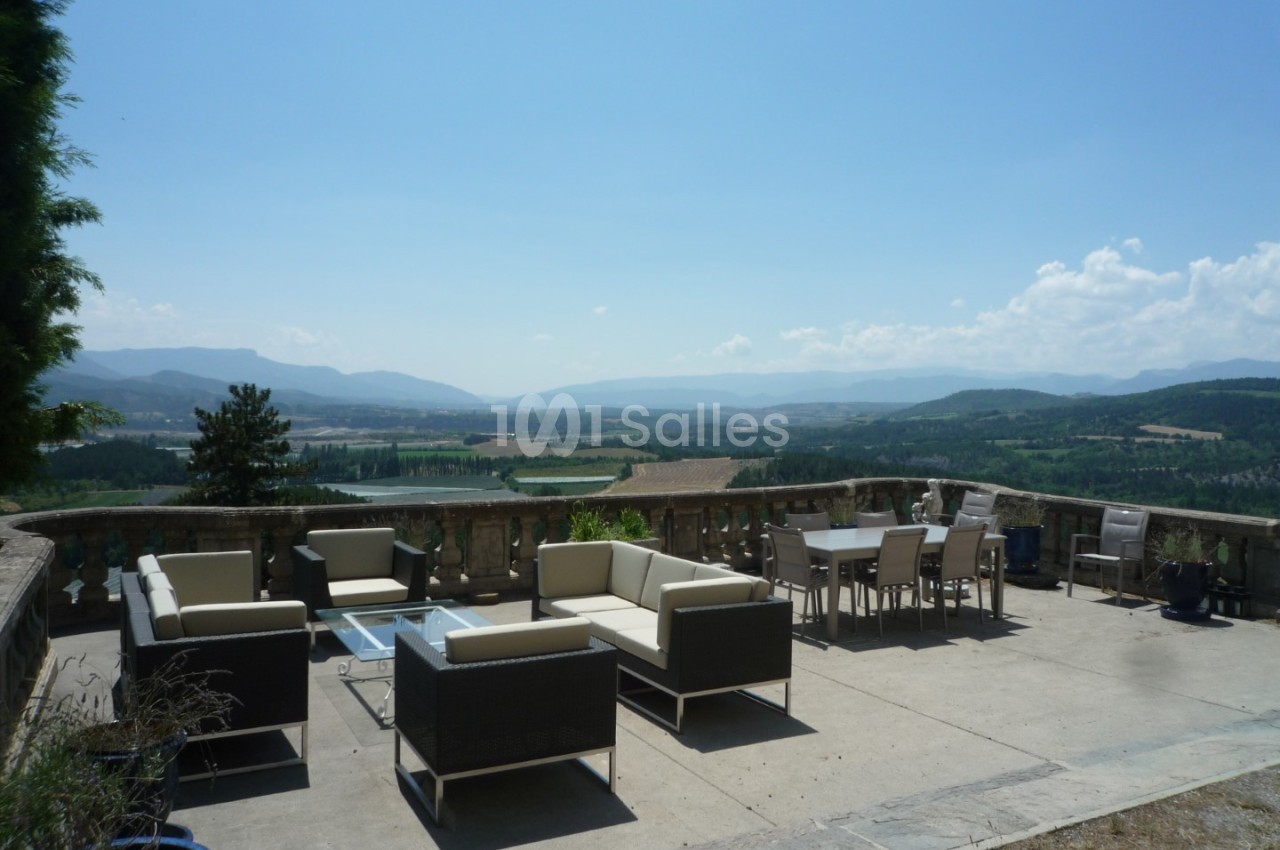 Terrasse meublée avec vue panoramique sur une vallée verdoyante et des collines sous un ciel dégagé.