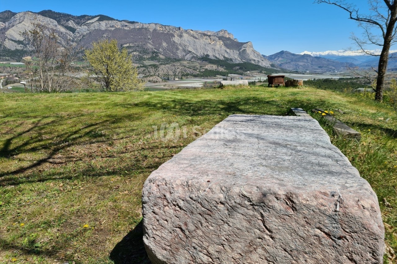 Bloc de pierre rectangulaire sur une pelouse avec vue sur des montagnes et un ciel dégagé en arrière-plan.