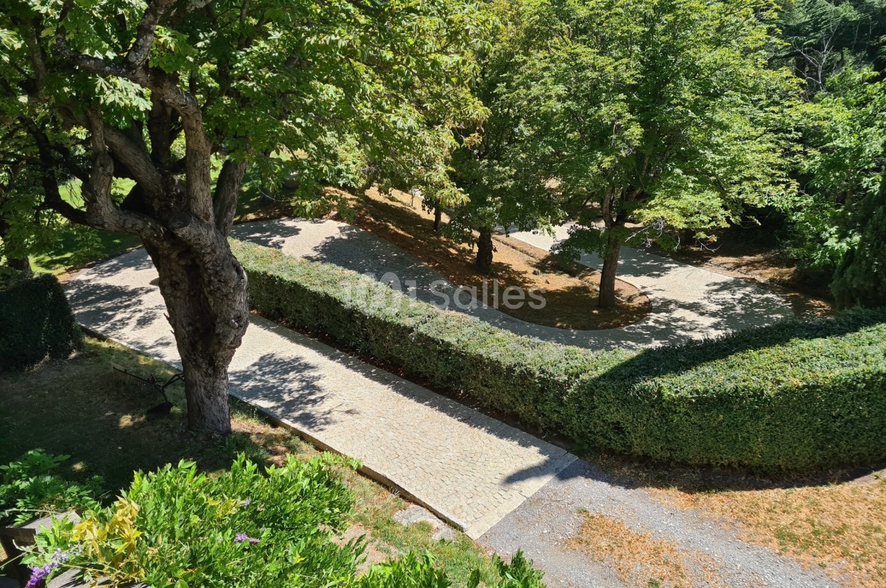 Allée pavée bordée de haies et d'arbres dans un jardin ensoleillé, vue depuis une hauteur.