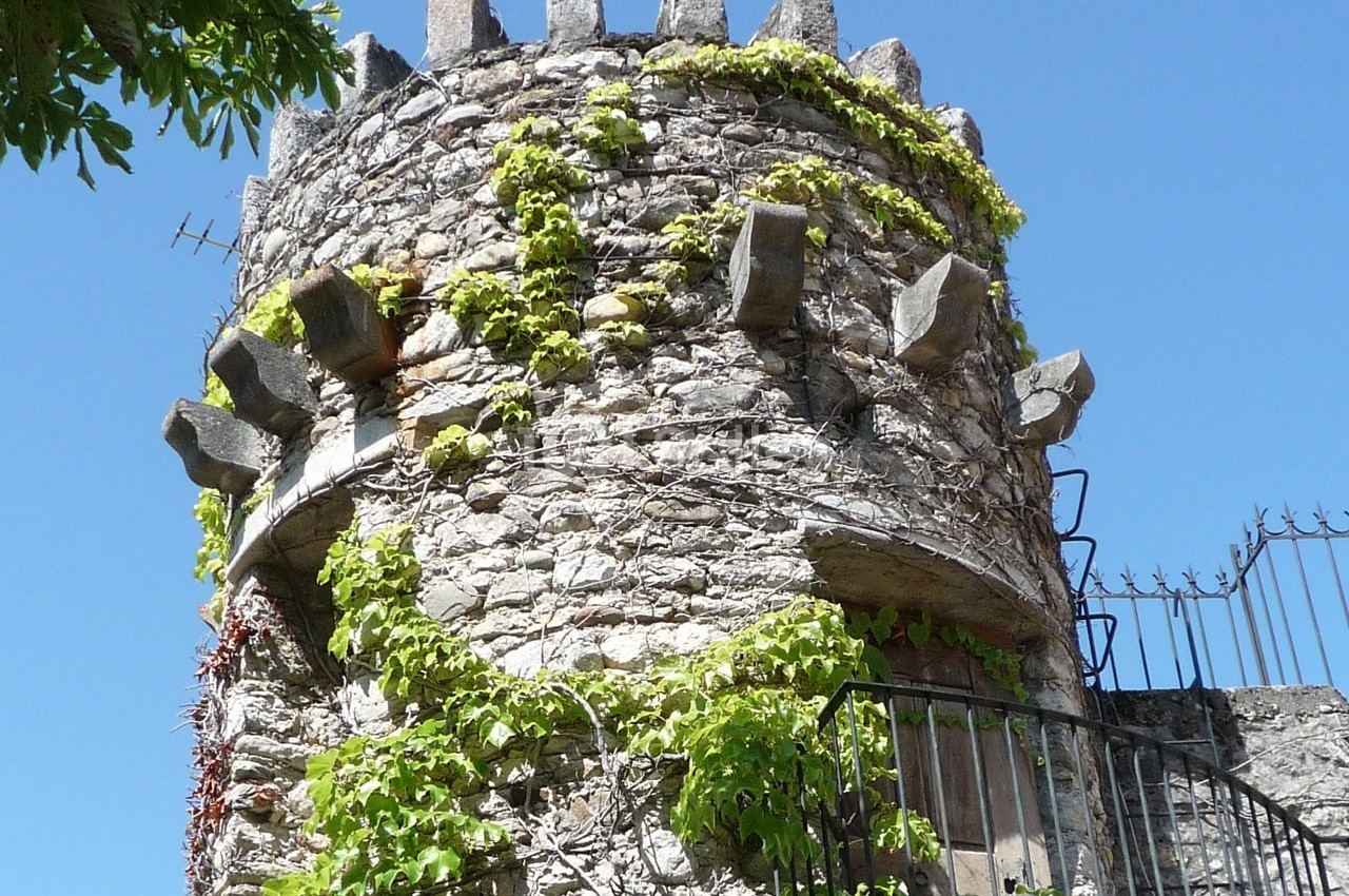 Tour en pierre ancienne recouverte de lierre, avec des créneaux et un ciel bleu en arrière-plan.