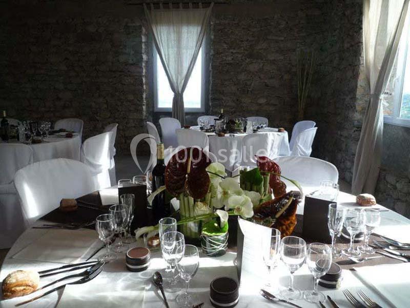 Salle de réception avec tables rondes dressées, nappes blanches, vaisselle élégante et centre de table floral.