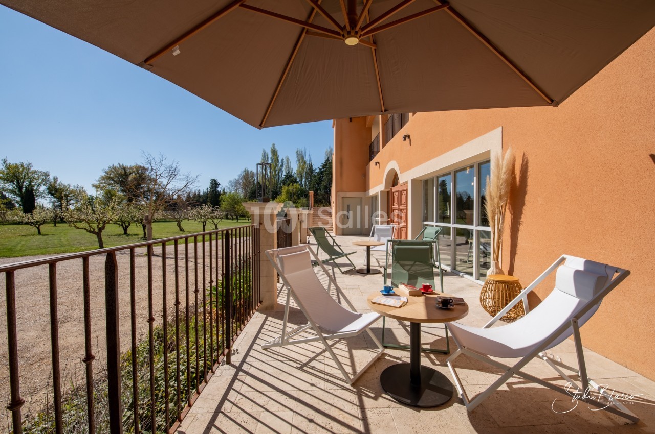 Terrasse ensoleillée avec chaises longues, table basse et parasol, donnant sur un jardin arboré.