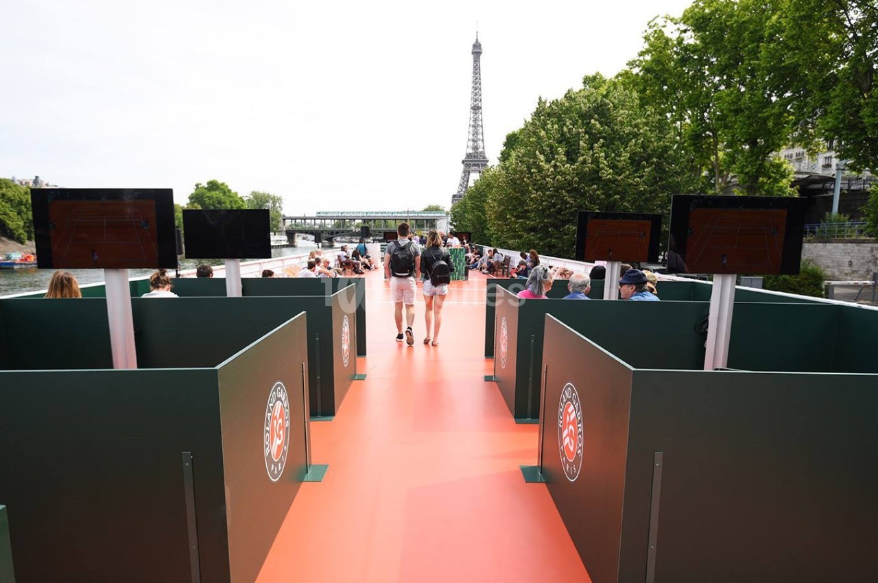 Passage piétonnier avec des panneaux Roland-Garros, vue sur la Tour Eiffel et la Seine en arrière-plan.