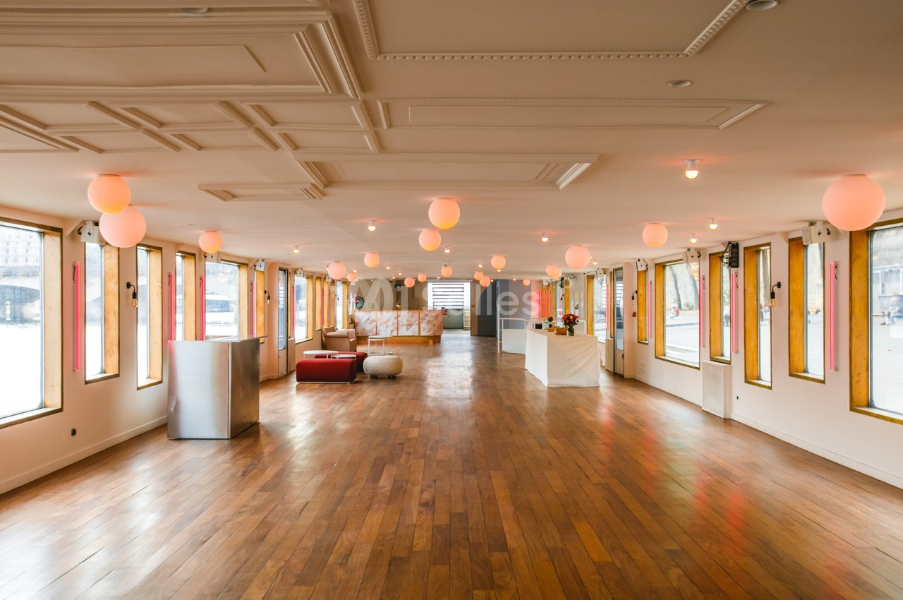 Salle spacieuse avec parquet en bois, grandes fenêtres, luminaires suspendus et mobilier minimaliste.