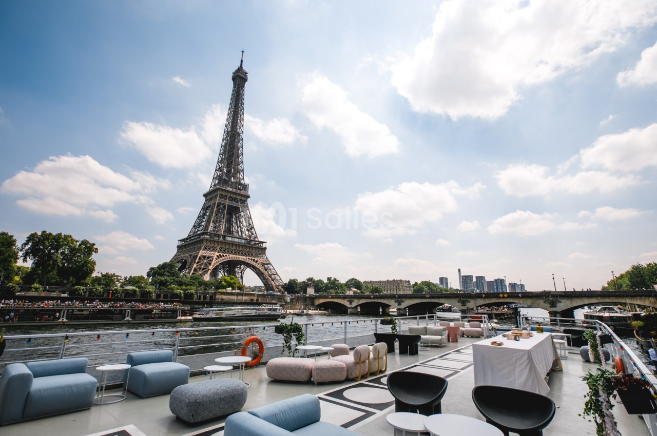 Vue de la Tour Eiffel depuis une terrasse aménagée au bord de la Seine par une journée ensoleillée.