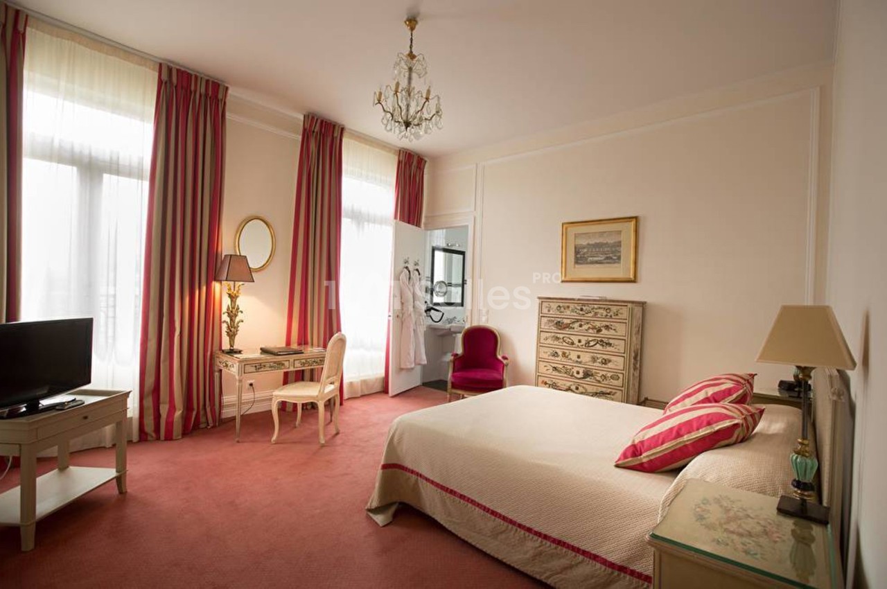 Chambre lumineuse avec lit double, bureau, fauteuil, commode et rideaux rayés, décorée dans un style classique.