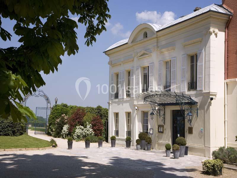 Façade d'un bâtiment élégant avec des volets blancs, une marquise en fer forgé et des plantes en pots devant l'entrée.