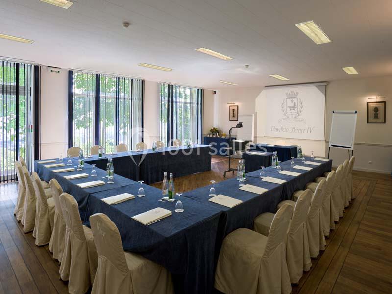 Salle de réunion lumineuse avec tables disposées en U, chaises couvertes, projecteur et tableau blanc.