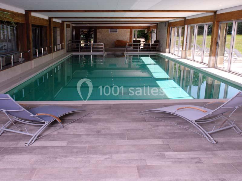 Piscine intérieure avec eau calme, entourée de baies vitrées et de chaises longues sur un sol en carrelage.