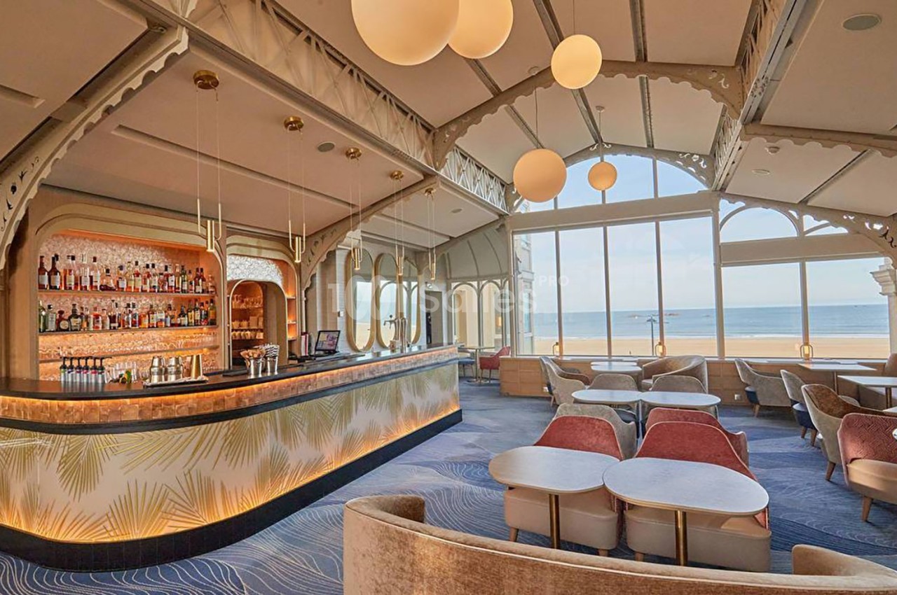 Intérieur d'un bar élégant avec vue sur la mer, grandes baies vitrées, mobilier moderne et éclairage chaleureux.