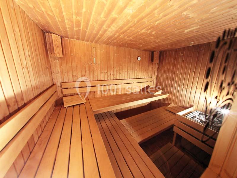 Intérieur d'un sauna en bois avec bancs disposés en gradins et un poêle visible dans un coin.