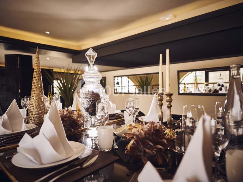 Table élégamment dressée avec serviettes pliées, chandeliers dorés, carafe en verre et décorations raffinées.
